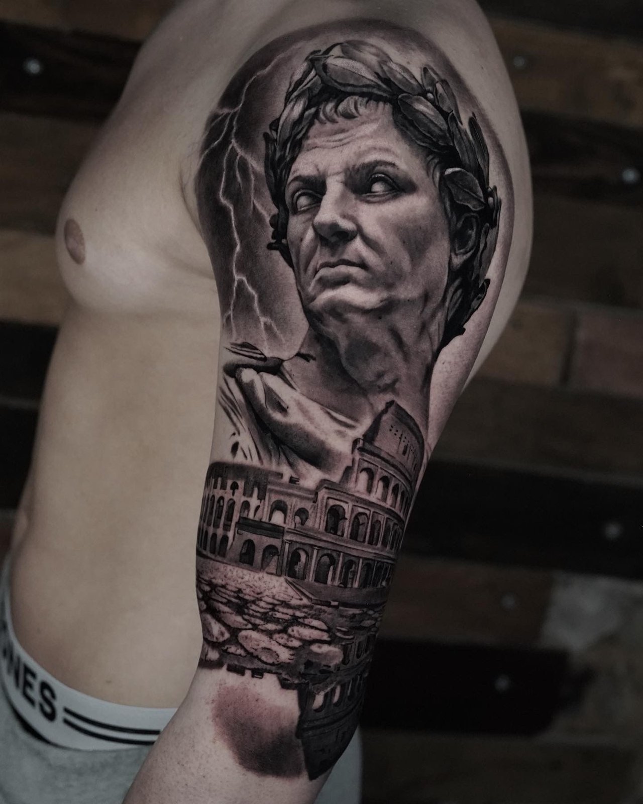 A man has a tattoo of a statue of a man and a building on his arm.